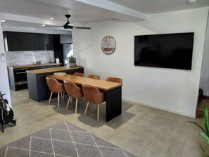 A modern kitchen with a dining area, a large TV, and a ceiling fan.