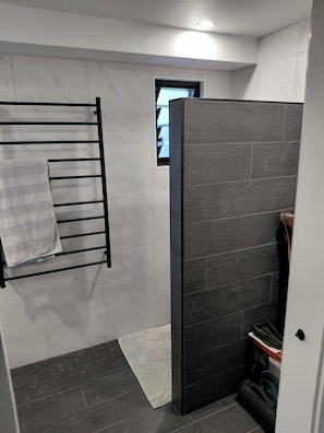 A bathroom with a towel rack, a small window, a dark tiled shower enclosure, and a white door.