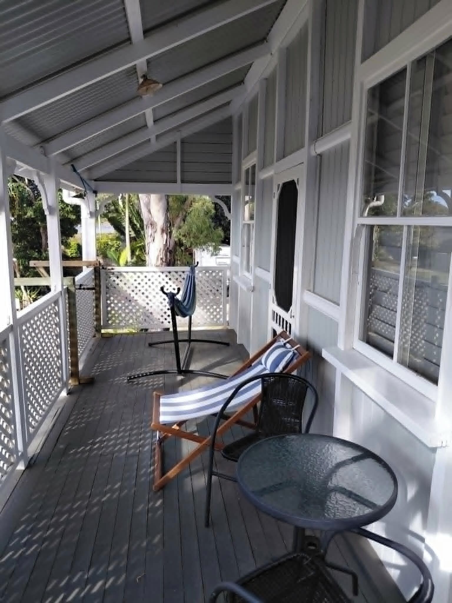 Une véranda avec une terrasse en bois, une chaise longue, une petite table et une vue sur l’extérieur.