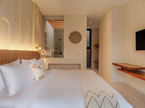 A modern hotel room with a large bed, a wooden headboard, a wall-mounted TV, and a mirror. - Villa Marma (Bali)