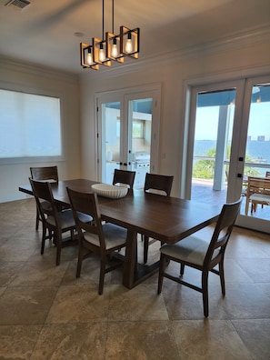 Un espace repas avec une table et des chaises en bois, un lustre moderne et une vue sur une terrasse extérieure, accessible par des portes vitrées.