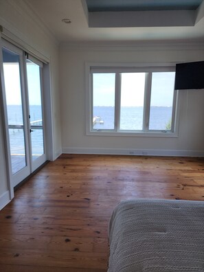 A room with a wooden floor, a large window with a view of the sea, and a ceiling with a blue accent. - Your Bayfront Retreat with Stunning Water Views, Private Pool, and Dock. (Gulf Breeze)