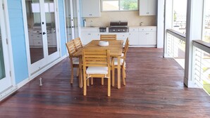 Un patio couvert avec une table et des chaises en bois, un ventilateur de plafond et un coin cuisine avec une fenêtre.