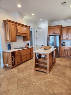 A kitchen with wooden cabinets, a stainless steel refrigerator, and a marble countertop. - Your Bayfront Retreat with Stunning Water Views, Private Pool, and Dock. (Gulf Breeze)