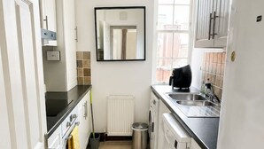 A compact kitchen with white cabinets, a built-in oven, a washing machine, and a window providing natural light. - 2bed Home With Free Parking Near Sydenham Station (London)