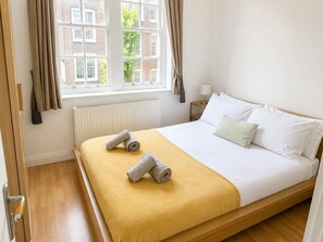 Ein Hotelzimmer mit Bett, einem fenster mit Vorhängen, einem Heizkörper und einem Nachttisch mit Lampe.