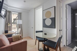 A modern hotel room with a round table, two chairs, a sofa, a TV, and a framed artwork on the wall. - Blueground | SoHo, view, nr Washington Square Park (New York)