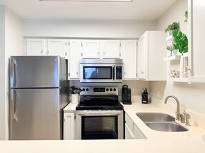 A modern kitchen with white cabinets, a stainless steel refrigerator, a microwave, a stove, and a sink. - Beach Front Paradise/Unobstructed Gulf View From Private Balcony/Pool (Destin)