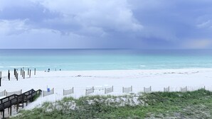 Ein Strand mit einem hölzernen Steg, der zum Wasser führt, feinem Sand und einem bewölkten Himmel.