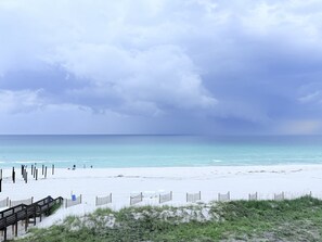 Ein Strand mit einem hölzernen Steg, der zum Wasser führt, feinem Sand und einem bewölkten Himmel.