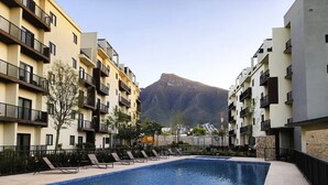 Une piscine entourée d’immeubles d’appartements dotés de balcons, une montagne en arrière-plan et un ciel dégagé.