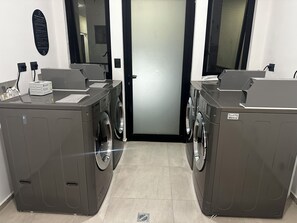A laundry facility with two washing machines, a control panel, and a door.