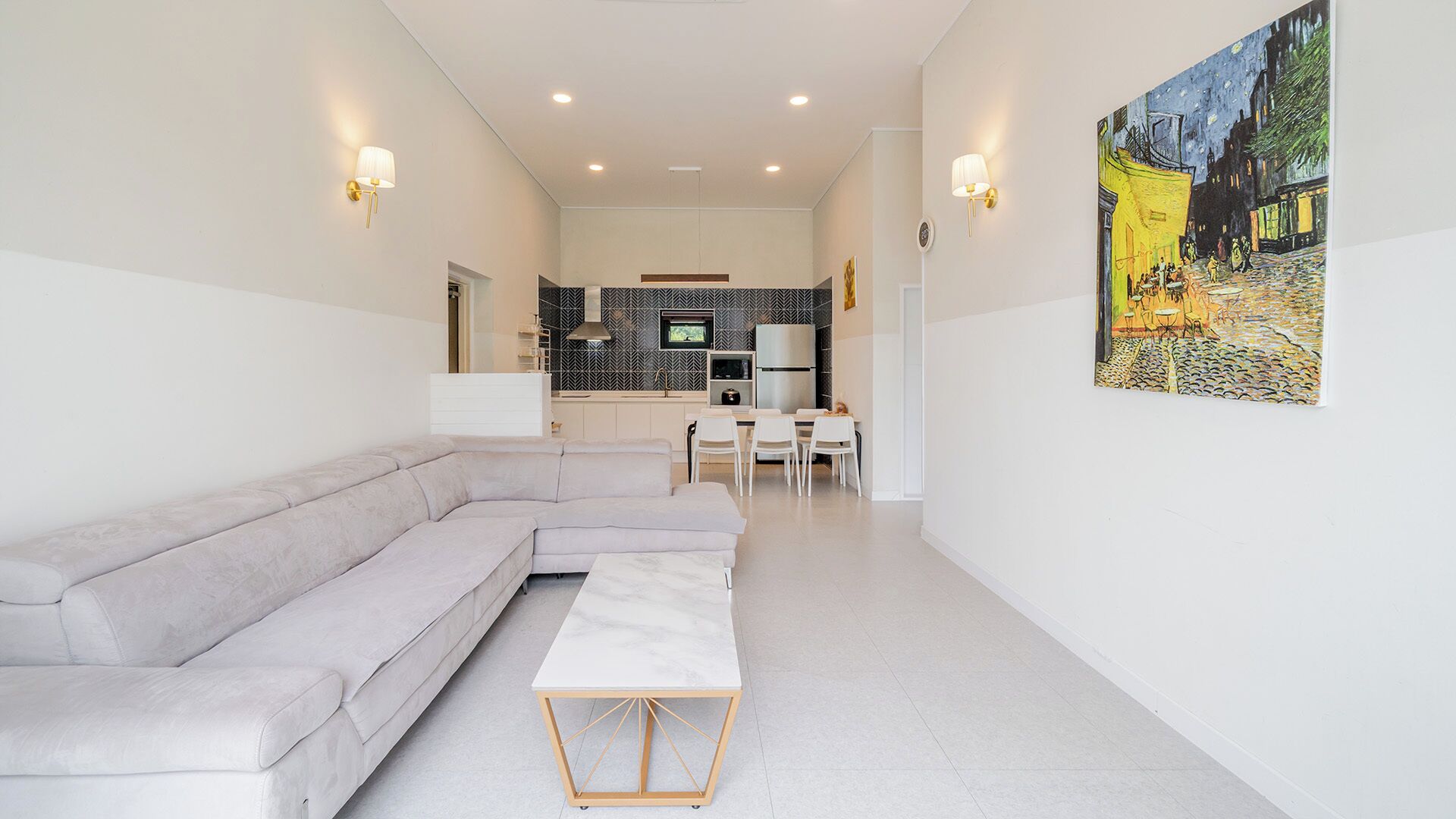 A modern living room with a sectional sofa, a small dining table, and a kitchen in the background.
