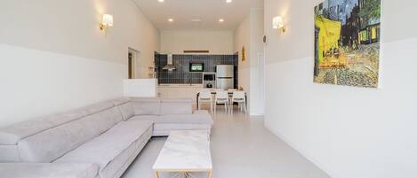 A modern living room with a sectional sofa, a small dining table, and a kitchen in the background.