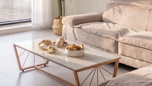 A modern living room with a beige sofa, a marble coffee table, and a bowl of snacks.