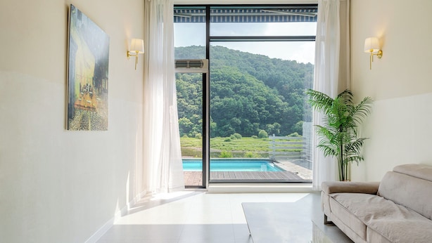 A room with a large sliding glass door leading to a pool, a painting on the wall, and a sofa.