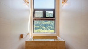 A bathroom with a bathtub, a window with a view of a forest, and wall-mounted lighting. - Hongcheon Around River Poolvilla Pension (Hongcheon)
