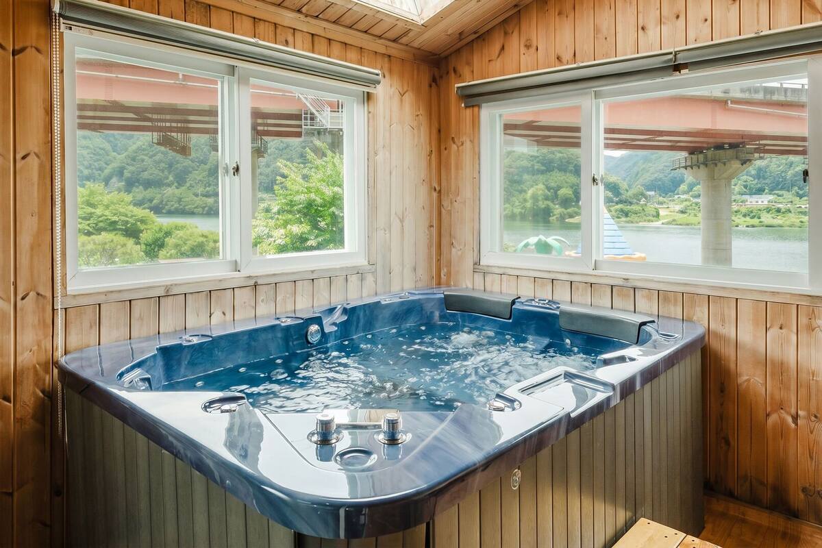 Una habitación de madera con bañera de hidromasaje, ventanas amplias y vistas a la vegetación.
