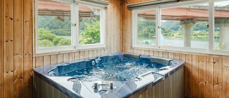 A wooden room with a hot tub, large windows, and a view of greenery.