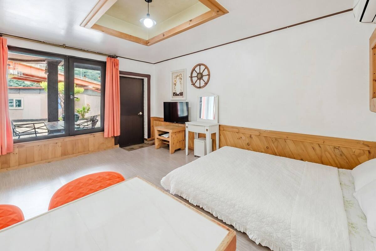 Una habitación con cama, escritorio, televisión y ventana con cortinas.
