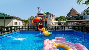 Piscina con toboganes y juguetes inflables, rodeada de edificios y una valla.