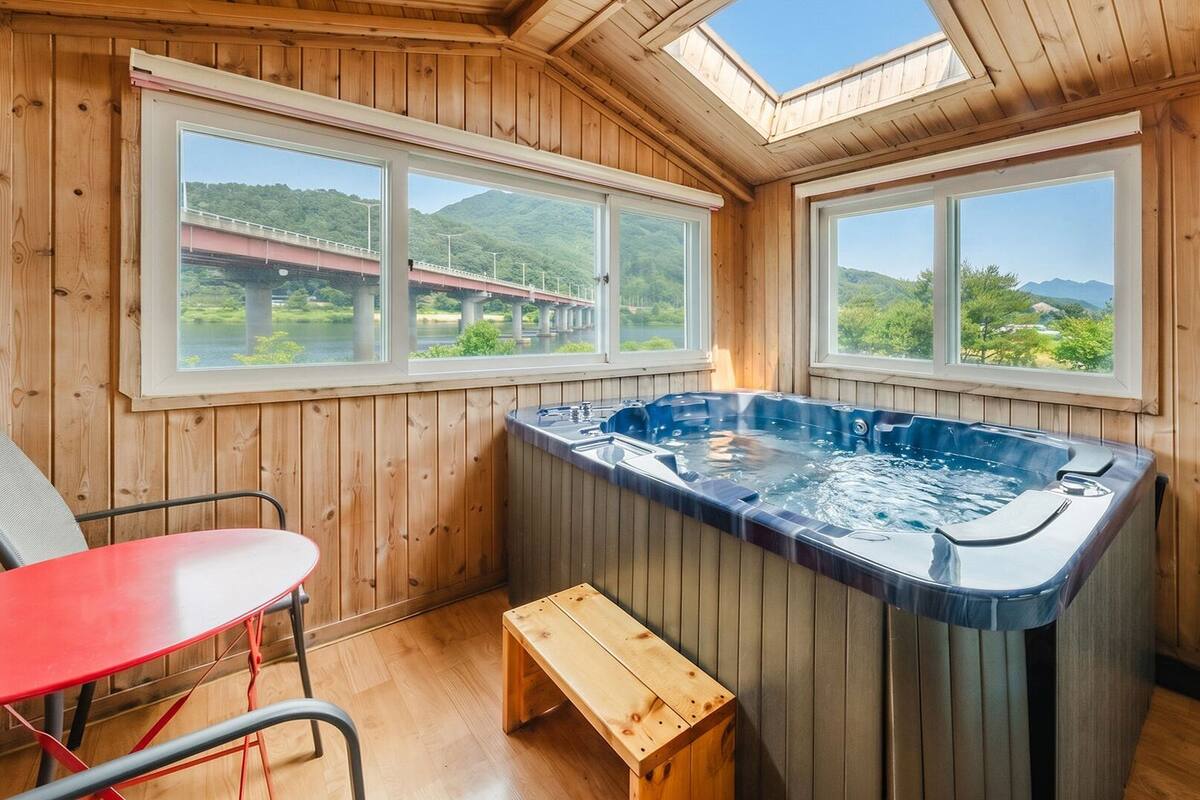 Una cabaña de madera con jacuzzi, dos ventanas, una mesa y un banco.