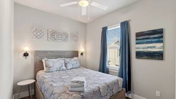 A bedroom with a bed, a ceiling fan, decorative wall art, a window with curtains, and a painting on the wall.