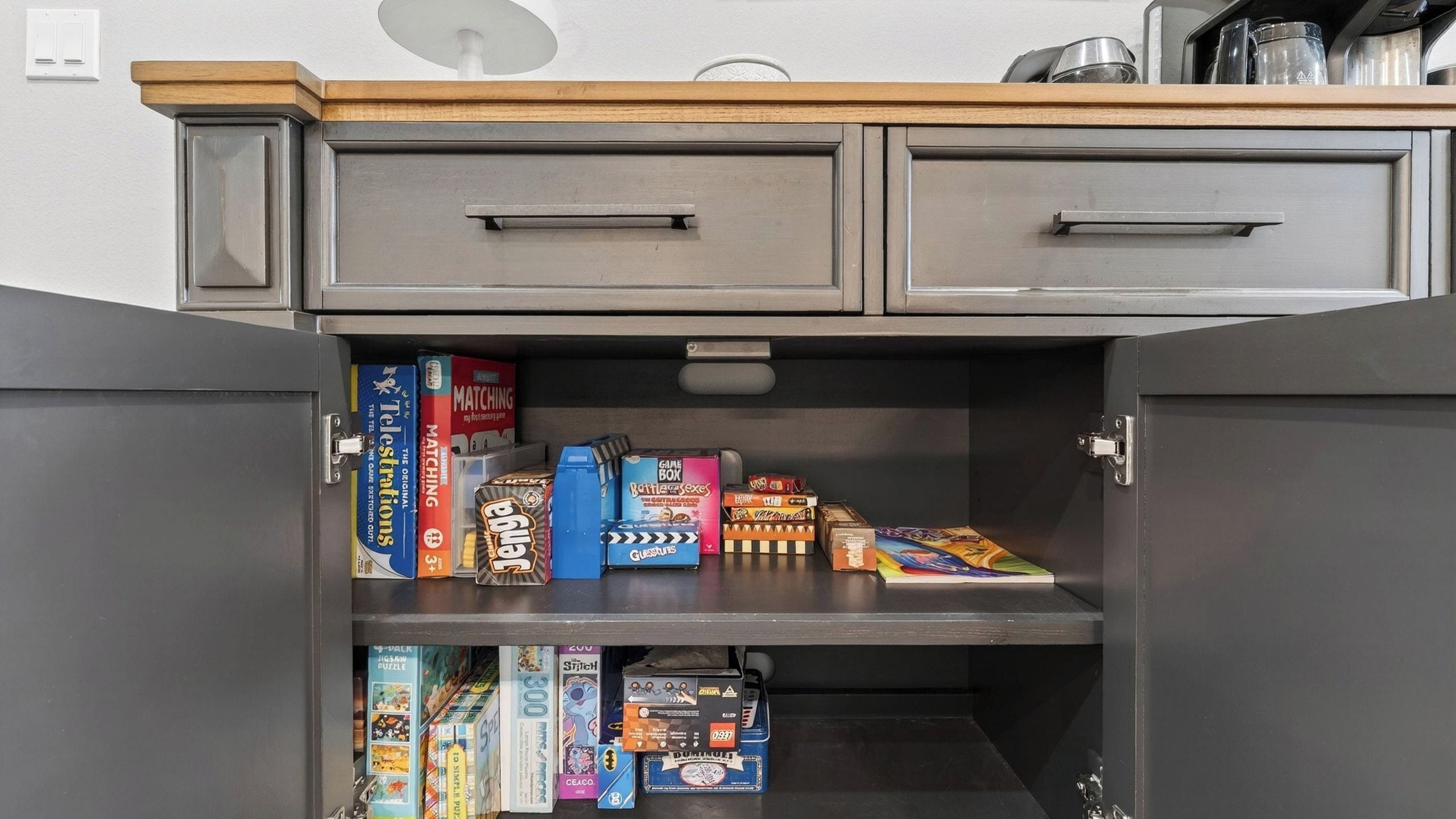 A kitchen cabinet with two drawers and a shelf containing various board games and puzzles.