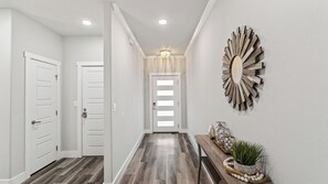 A hallway with a wooden floor, white doors, a decorative mirror, and a light fixture.