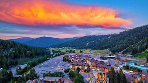 A town with a parking lot, buildings with multiple stories, and a mountainous backdrop.