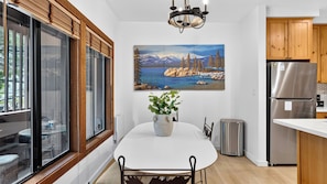 A modern kitchen with a dining table, a painting of a mountainous landscape, and wooden cabinets.