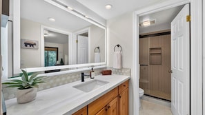 A bathroom with a large mirror, a sink, wooden cabinets, a towel rack, and a shower area.