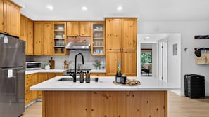 Eine moderne Küche mit Holzschränken, einem Edelstahlkühlschrank, einer eingebauten Mikrowelle und einer großen Kochinsel mit Spüle.