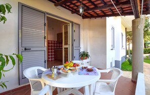 A patio with a round table, white chairs, and a breakfast spread including fruits, pastries, and coffee. - Apartment in Ricadi (047) (Ricadi)