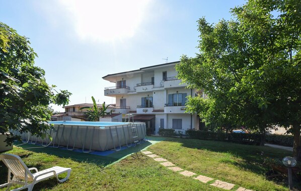 A multi-story residential building with a swimming pool, a garden, and a clear sky. - Apartment in Ricadi (047) (Ricadi)