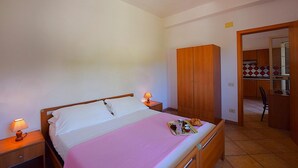 Une chambre à coucher avec un lit, des lampes de chevet, une armoire en bois et une salle de bain visible à travers une porte ouverte.