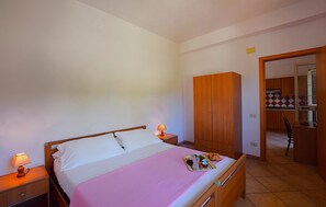 A bedroom with a bed, bedside lamps, a wooden wardrobe, and a bathroom visible through an open door. - Apartment in Ricadi (047) (Ricadi)