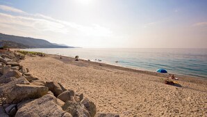 Une plage avec de gros rochers au premier plan, un ciel dégagé et une mer calme.