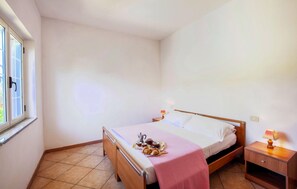 Ein Einzelbett mit Holzrahmen, ein Nachttisch mit Lampe sowie ein Fenster mit Blick auf Grünflächen.