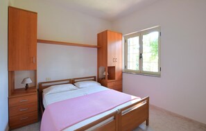 Ein Schlafzimmer mit Bett, Holzschrank, Nachttisch, Lampe und Fenster mit Blick.