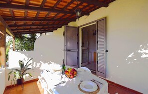 Eine Terrasse im Freien mit Esstisch, einem Blumentopf und einer Tür mit Rollläden.