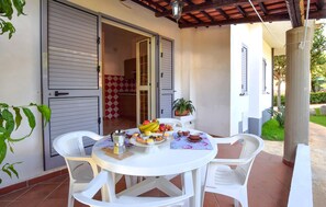 Eine Terrasse mit rundem Frühstückstisch, weißen Kunststoffstühlen und Blick ins Hausinnere.