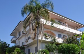 Un immeuble à plusieurs étages doté de balcons, d’un palmier et entouré de verdure.