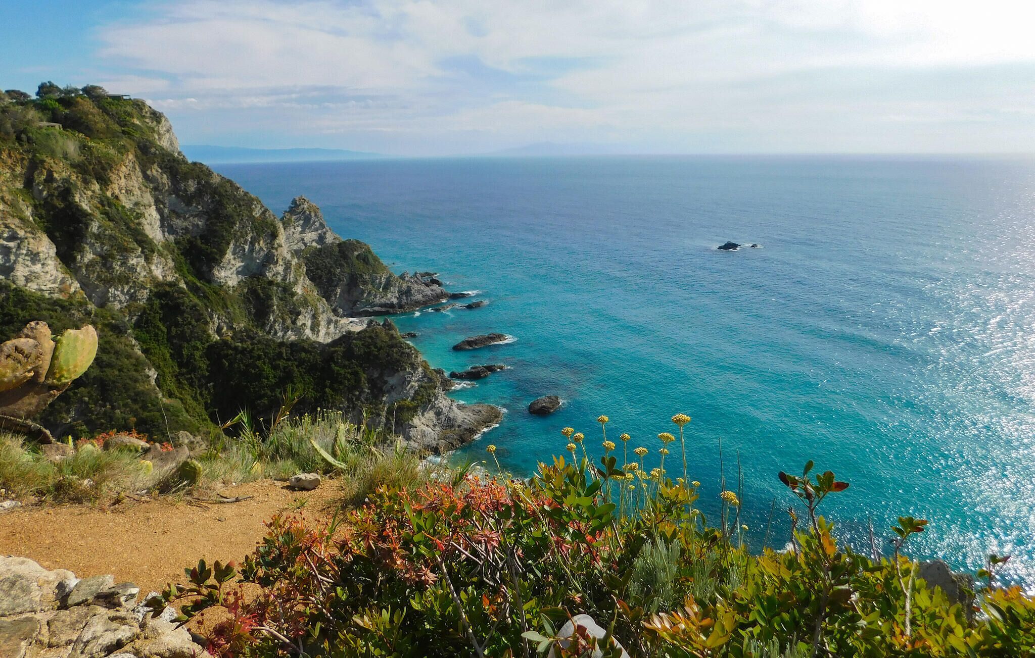 Paisaje costero con vista despejada al mar, acantilados rocosos y un sendero que conduce al agua.