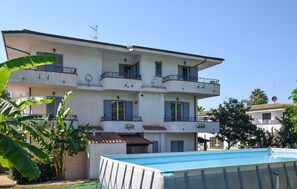 Un immeuble résidentiel à plusieurs étages, doté de balcons, d’une piscine et entouré de verdure.