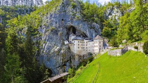 Un castello incastonato in una rupe rocciosa con un paesaggio verdeggiante.