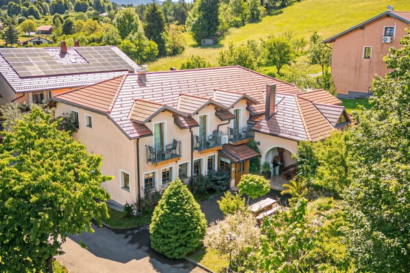 A large, multi-story house with a red-tiled roof, multiple balconies, and a well-maintained garden.