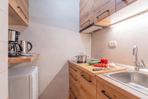 A modern kitchen with wooden cabinets, a stainless steel sink, and a countertop with a kettle, pot, and vegetables. - Pivka Apartment With 2 Balconies, Pivka, Slovenia (Pivka)