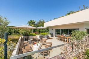 Un patio exterior con mobiliario de mimbre, sombrillas y una zona de barbacoa.