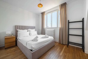 A modern bedroom with a bed, bedside table, lamp, window, and a black metal shelf. - Bright 1BDR Retreat in Paris 15th (Paris)